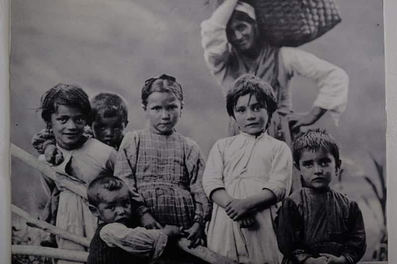 Foto eines Fotos: Jerome Mintz, der immer verfolgt von den Franco-Faschisten, mit den Anarchist_innen von Casas Viejas Kontakt hielt. Das Foto zeigt fünf Kinder im Vordergrund mit unterschiedlichen Gesichtsausdrücken. Dahinter steht eine junge Erwachsene mit einem geflochtenen Korb, der mit einer Hand von der Schulter bis über den Nacken getragen wird. Das monochrome Bild vermittelt den Eindruck eines harten und ärmlichen Lebens. Die Position des Fotografen ist so gewählt, dass die Kamera nach oben blickt und gibt den Kindern Würde und zeigt Respekt.